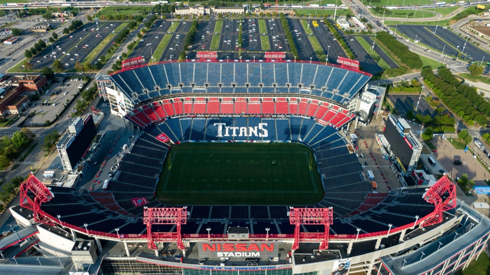 Aerial view of an open-air stadium, its tiered seating bowl wrapped around a turf pitch, with car parks and access roads spread around it