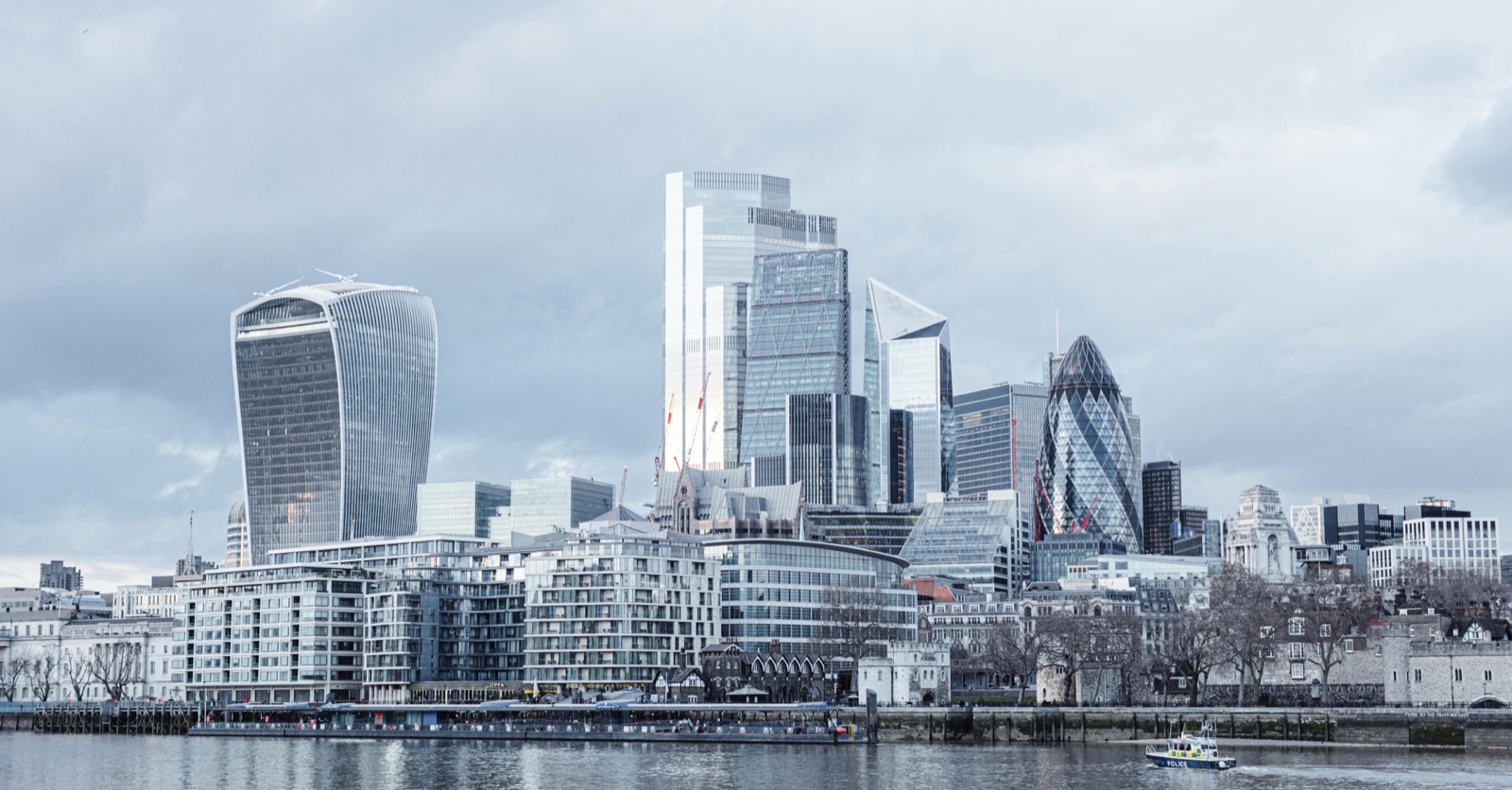 The City of London skyline across the Thames under grey cloud, the Walkie-Talkie and the Gherkin among the towers with the Tower of London in front