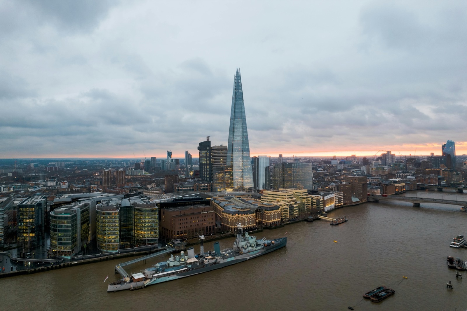 London from above at dusk, the Shard rising over the south bank with the Thames curving past moored ships and riverside offices