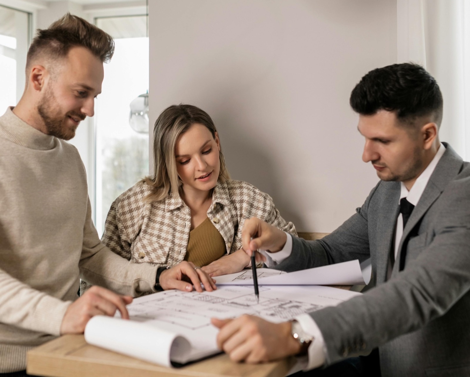 Two clients and an engineer leaning over floor plans spread across a table, the engineer pointing at a detail with a pencil